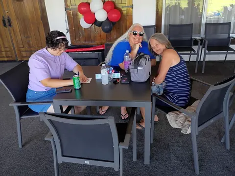 Three guests seated around a patio table beneath red, white and black balloons.