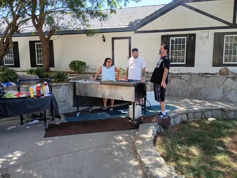 Three people gathered around an outdoor grill beside the clubhouse.