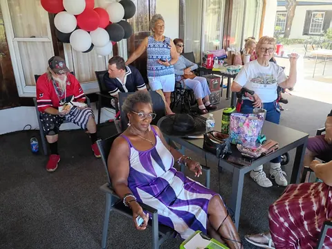 Guests gathered beneath balloons, with a guest in a purple-and-white dress in front.