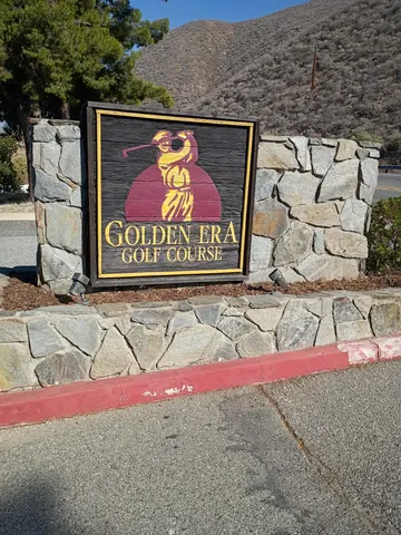 Golden Era Golf Course sign on a stone wall with hills behind it.