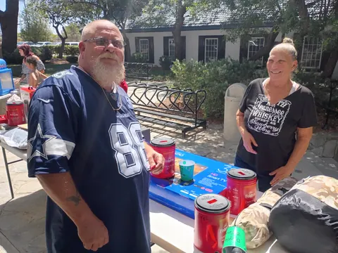 Two guests beside raffle containers and boxed prizes on an outdoor table.