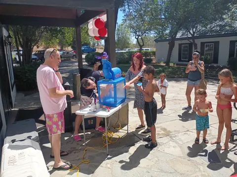 Adults and children gathered around a blue snow-cone machine outdoors.